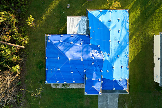 Blue protective tarps covering a storm-damaged roof